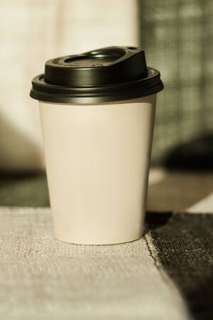 Kraft paper coffee cup with black lid from street shop with hot aroma drink near the window. Lifestyle concept, take away food. Copy space, front view.の写真素材