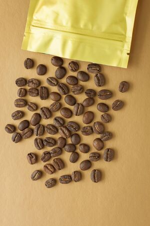 Gold foil bag with coffee beans on golden background. Packaging template mockup. Aluminium package for tea, flatlay.の写真素材