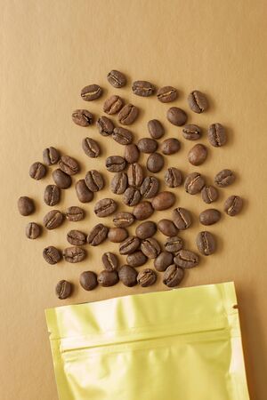 Gold foil bag with coffee beans on golden background. Packaging template mockup. Aluminium package for tea, flatlay.の写真素材