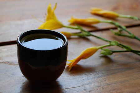Green tea bowl on a dark brown wooden background with beautiful yellow lilies.の写真素材