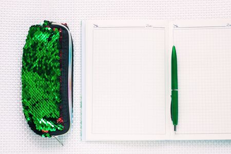Opened notebook, fashion pencil case with sequins and green pen on white textured background. Minimal work space, stylish stationery, office tools, working and educational supplies. Top view,flat lay.の写真素材