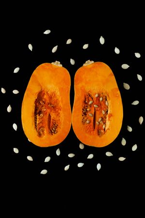 Two halves of a pumpkin with seeds on a black background. Creative minimalism, dark and moody food photography. Copy space, squash top view, flat lay. Halloween concept.の写真素材
