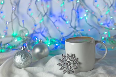 Christmas coffee cup with new year decorations on background. Winter holidays card, cozy home concept, festive wallpaper. White mug with hot drink. Copy space with bokeh lights.の写真素材