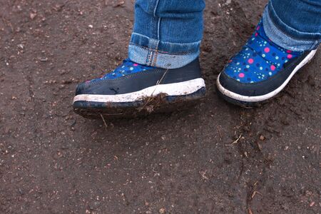 Kids boots in muddy puddle. Colorful winter outdoor rain shoes on childrens feet in action. A child on a walk stay in the mud. Choosing footwear for an active lifestyle. Autumn rainy weather.の写真素材