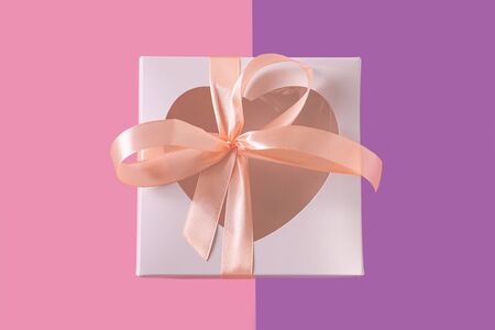 White gift box with heartshaped window on pastel purple background flatlay, creative minimal concept. Transparent heart, pink ribbon bow. Valentines day cards. Top view,copy space,social media bannerの写真素材