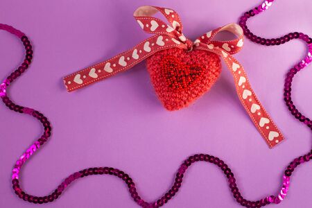 Pink knitted heart on pastel purple background flatlay, creative concept. Cute decorative heartshaped pillow with sequins ribbon bow. Valentines card, gift. Top view, copy space, social media banner.の写真素材