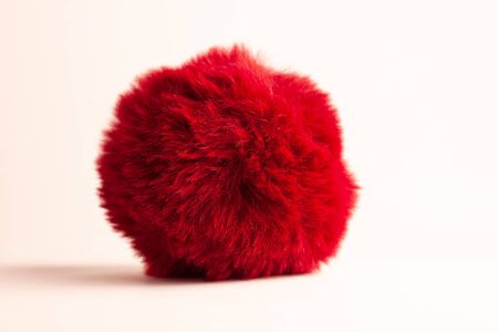 Red fur ball isolated on white background with natural shadow. Keychain, hats fashion style accessory, bag and backpack decoration. Girl clothes wardrobe,female style. Copy space.の写真素材