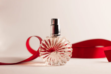 Creative perfume bottle with red silk ribbon on white background. Blank perfumery mockup, spa branding concept.Glamour fragrance, eau de parfum.Holiday gift banner.Luxury beauty cosmetics brand designの写真素材