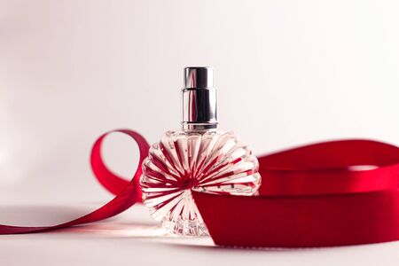 Creative perfume bottle with red silk ribbon on white background. Blank perfumery mockup, spa branding concept.Glamour fragrance, eau de parfum.Holiday gift banner.Luxury beauty cosmetics brand designの写真素材