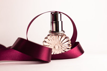 Creative perfume bottle with red silk ribbon on white background. Blank perfumery mockup, spa branding concept.Glamour fragrance, eau de parfum.Holiday gift banner.Luxury beauty cosmetics brand designの写真素材