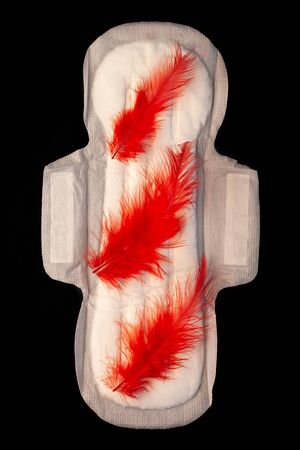 Menstrual pad with red feathers like blood drops on black background top view. Irregular period concept. Menorrhagia heavy menstruation bleeding. Critical days hygiene product.Creative minimal flatlayの写真素材