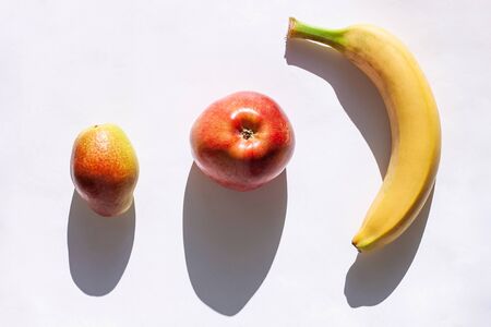 Creative healthy breakfast concept on a white background flat lay. Fresh banana, apple, pear fruits with shadow. Vitamins minerals,dietary fiber rich food top view,copy space.Delicious snack, smoothieの写真素材