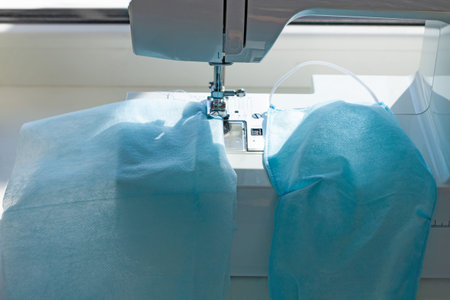 Handmade sew the face mask against coronavirus disease COVID-19 pandemia. Sewing machine with...