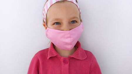 Little girl in headband wearing protective pink fabric mask against coronavirus COVID-19 pandemic white background.virus epidemic.Children's handmade protection with sewn masks during quarantineの写真素材
