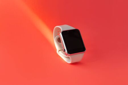 Smart watch with white silicone band side view on pink coral background. Trendy sports style watches on bracelet, waterproof wristband for active people with pedometer, heart rate and sleep monitoringの写真素材