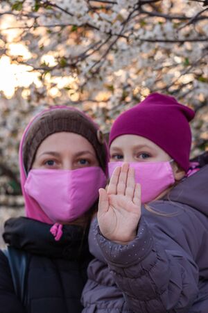 Mother and daughter wearing pink protective face mask against COVID-19 coronavirus disease. Stop epidemic hand gesture. Mom and child in surgical masks on empty city streets nature. Virus protection.の写真素材