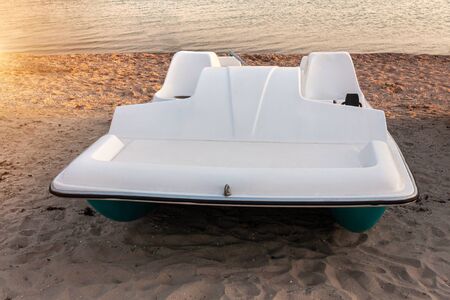 Pedal boats on the sunset on a tropical island beach. White catamaran on an empty sea shore on evening landscape with sun rays. Wallpaper for desktop, poster, marine travel photo, post card design.の写真素材