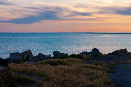 Amazing colorful sunset on an empty beach. Orange and red shades on the sky. Deserted shore with windmills on a background. Wallpaper for desktop, poster, marine travel photo for post card design.の写真素材