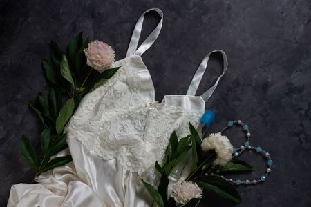 Woman's glamour white lingerie and jewelry accessories with peony flowers on dark background. Female fashion blog flat lay social media copy space. Lace underwear sexy silk night dress top view.の写真素材