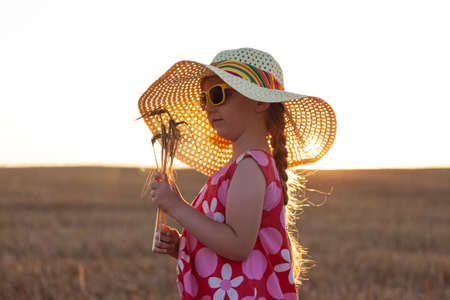 Adorable little girl in a straw hat and pink summer dress in wheat field. Child with long blonde hair on sunset on a countryside landscape with bunch of spikelets in hands. Farming agriculture conceptの写真素材