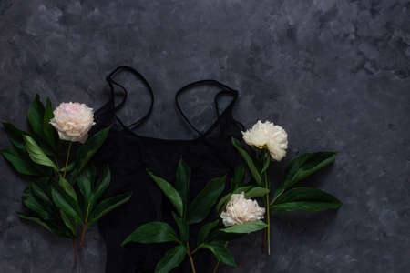 Woman's glamour black lingerie and jewelry accessories with white peony flowers on dark background. Female fashion blog flat lay social media copy space. Lace underwear sexy night clothes top view.の写真素材