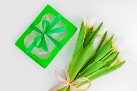 White tulip flowers and green gift box with ribbon bow on light background flat lay. Place for text...