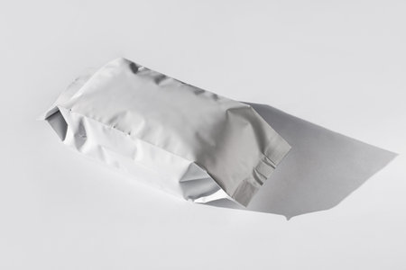 Blank foil food or drink bag on white background in minimal style, natural light shadow. Monochrome...