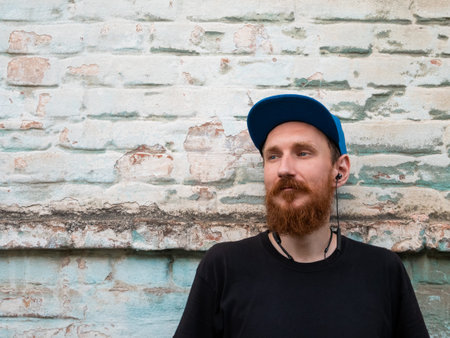 Portrait of young red bearded man in black t-shirt and snapback in rock style on urban background...