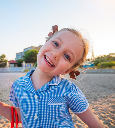Portrait of a beautiful liitle girl in blue plaid summer dress with blonde hair close-up. Joyful...
