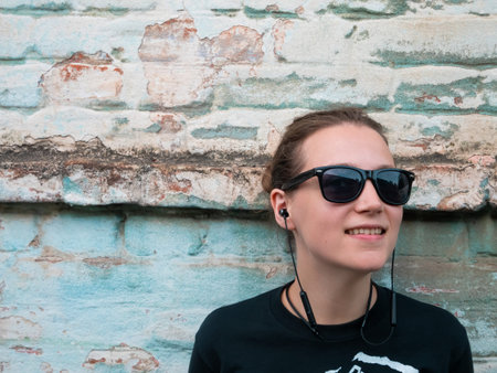 Portrait of young attractive girl in black t-shirt and sunglasses in rock style on urban background...