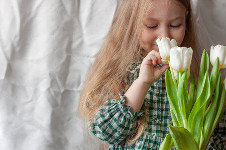 Cute blonde child girl with bouquet of white tulips in hands. Mothers day, spring concept. Pretty...