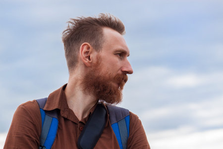 Handsome hipster man with lush beard and mustache on blue cloudy sky background. Red bearded guy...
