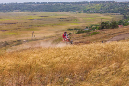 Motorcyclist rides on a wild hills. Motocross bike on beautiful rural landscape witj cloudy sky on background. Red motorcycle off-road outdoors. Berdyansk Ukraine - 06 september 2020のeditorial素材
