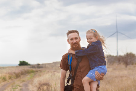 Father with daughter in hands standing on a hill with nature lanscape. Little blonde girl smiling...