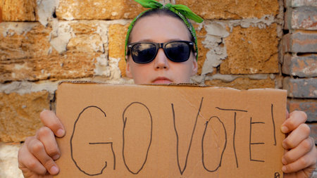 Girl shows cardboard with Go Vote sign on brick wall urban background. Voting concept. Make the...