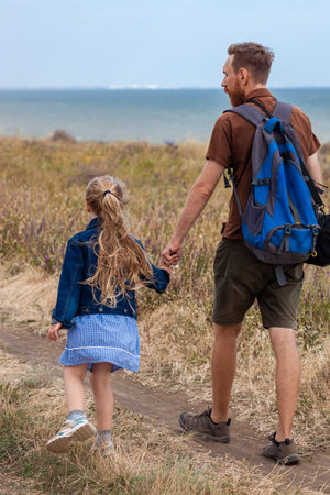 Father with daughter by the hand standing on a hill with nature lanscape. Little blonde girl hugging...