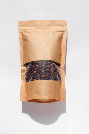 Brown kraft paper pouch bags with coffee beans top view with shadow isolated on white background....