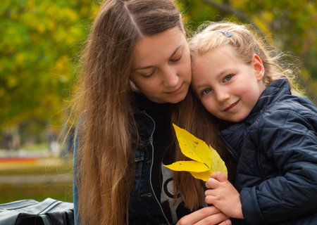 Cheerful mother and daughter smiling sitting in autumn park. Happy family walk. Cute little child...