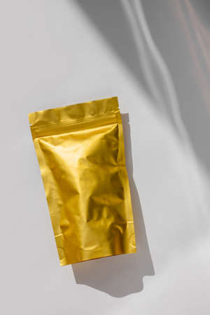 Golden metalized pouch bags with coffee beans top view with natural shadow isolated on white background. Packaging for food template mockup. Packs with clasps for tea leaves, weight products flat lay.の写真素材