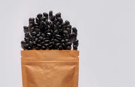 Kraft paper pouch bag with black beans top view with harsh shadow white background. Raw black gram Vigna Mungo packaging template mockup flat lay. Dieting nutrition concept, vegan protein source foodの写真素材