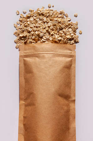 Brown kraft paper pouch bags with oats top view with harsh shadow on white background. Oatmeal cereal porridge pack flat lay. Rolled oat flakes packaging, healthy vegan food template mockup for designの写真素材