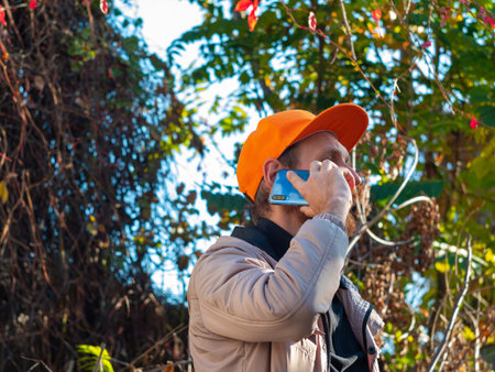 Young red bearded man speaks on mobile phone smiles. Guy in raincoat and orange cap on colorful...
