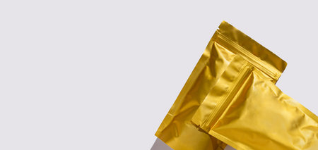 Golden metalized pouch bags mockup with coffee beans top view with harsh shadow isolated on white...