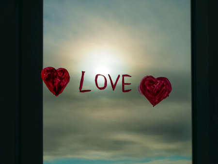 Drawing red heart on window glass with paints. Valentine's day greeting card template, love, dating, quarantine family leisure. Stay home art concept. Child painting playing indoors. New normal.の写真素材