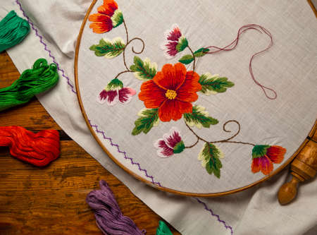 Flowers embroidery on white textile in hoop wooden background. Traditional ukrainian floss stitch embroidery motifs. Handmade ethnic clothes towel tablecloth. New normal lockdown hooby crafts tutorialの写真素材