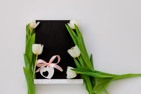 Black chalk board mockup with tulip flowers on white background. Blackboard menu with easel, spring sales. Copy space frame ad text content. Blank inscription template. Education advertisement displayの写真素材