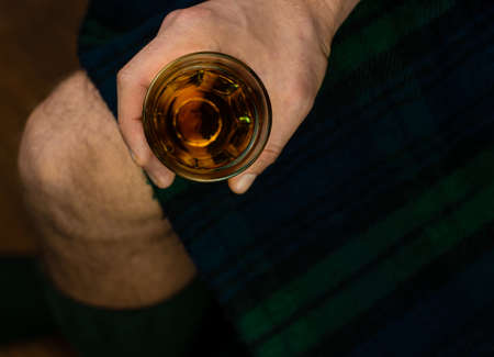 Irish man in traditional green kilt celebrating St. Patrick's Day with scotch drink glass in hand. Scottish guy drinking whiskey in pub minimal style 17 March cultural grand parade celebration Irelandの写真素材