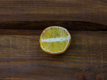 Ugly food trend. Spoiled yellow lemon half with red mold close up on wooden background. Moldy citrus penicillin unhealthy inedible fruit. Dangerous toxic harmful product, laboratory scientist researchの写真素材