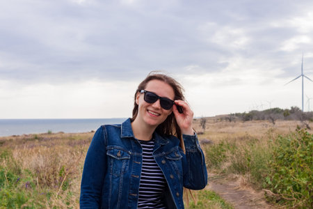 Woman in denim jacket on hill with wild grass and blue sea background. Stylish girl with long...