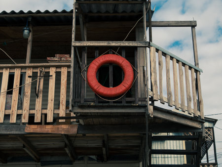 Old retro red lifebuoy hanging on wooden balcony. Help, rescue concept. Marine wallpaper copy space. Vintage life saver on the wood beach house on a sunny day. Travel lifestyle photo.の写真素材
